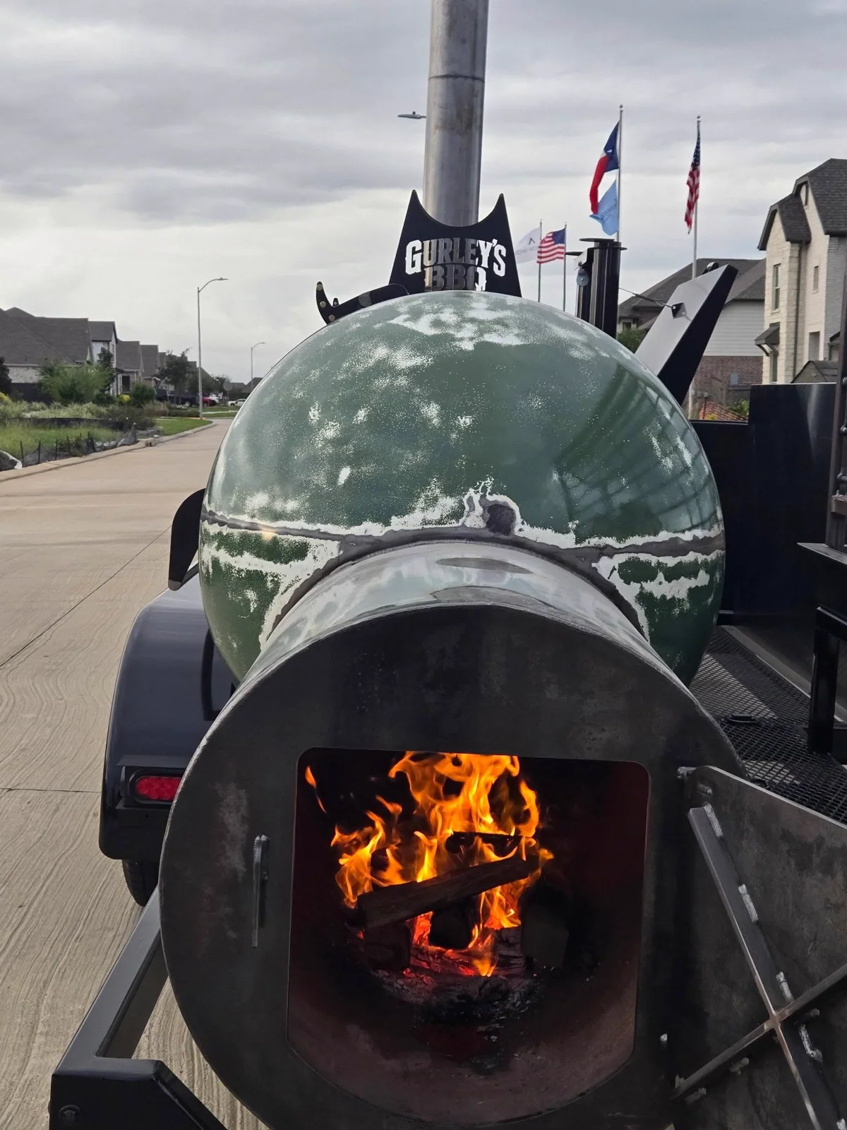 A live fire burning in the open firebox of Gurley’s green smoker
